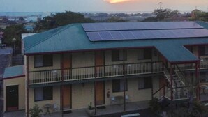 Een motel met twee verdiepingen, een groen dak en zonnepanelen, met een parkeerplaats en uitzicht op de ondergaande zon.