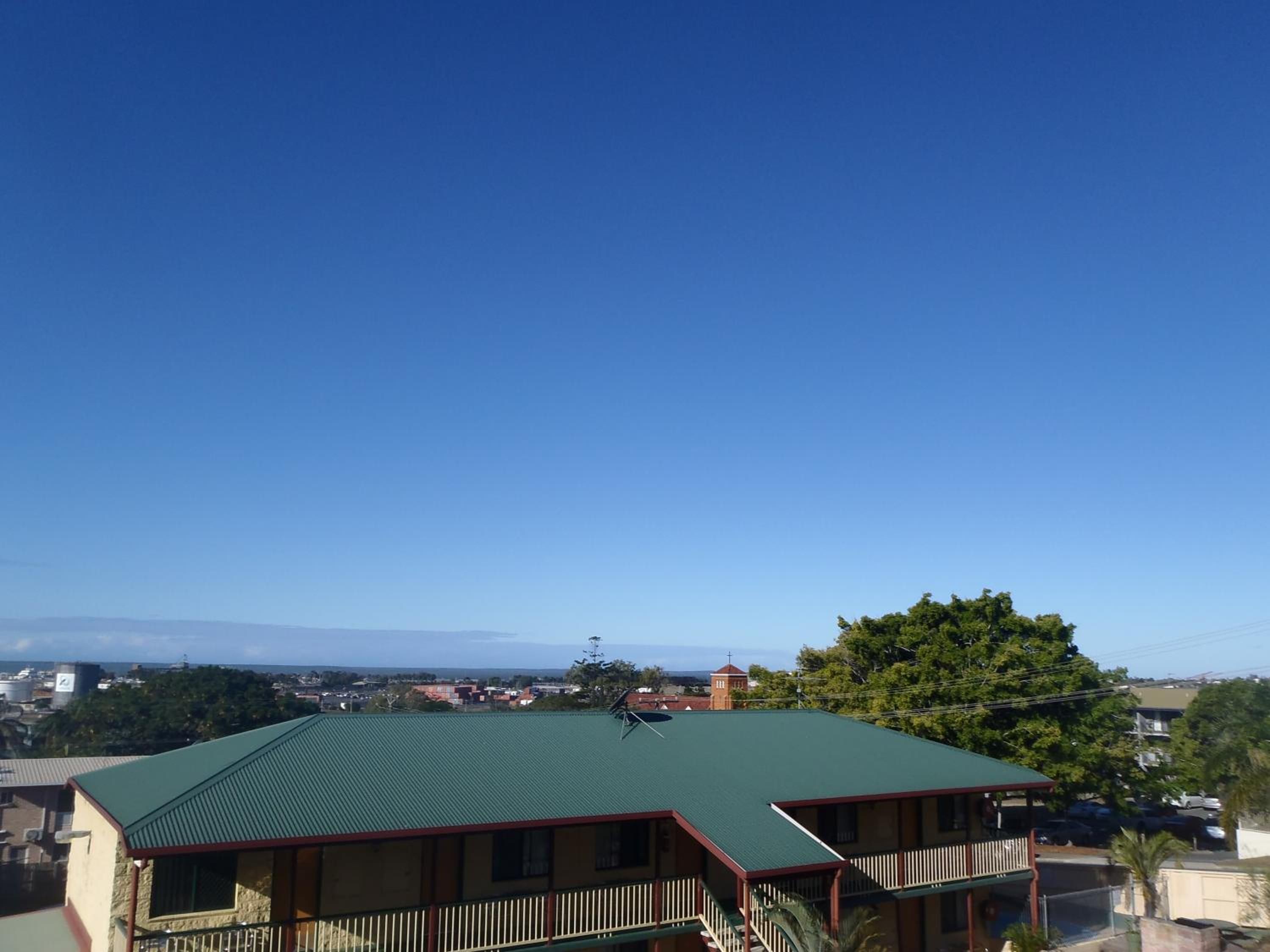 A building with a green roof, a balcony, and a view of a town and mountains in the distance.