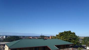 A building with a green roof, a balcony, and a view of a town and mountains in the distance.