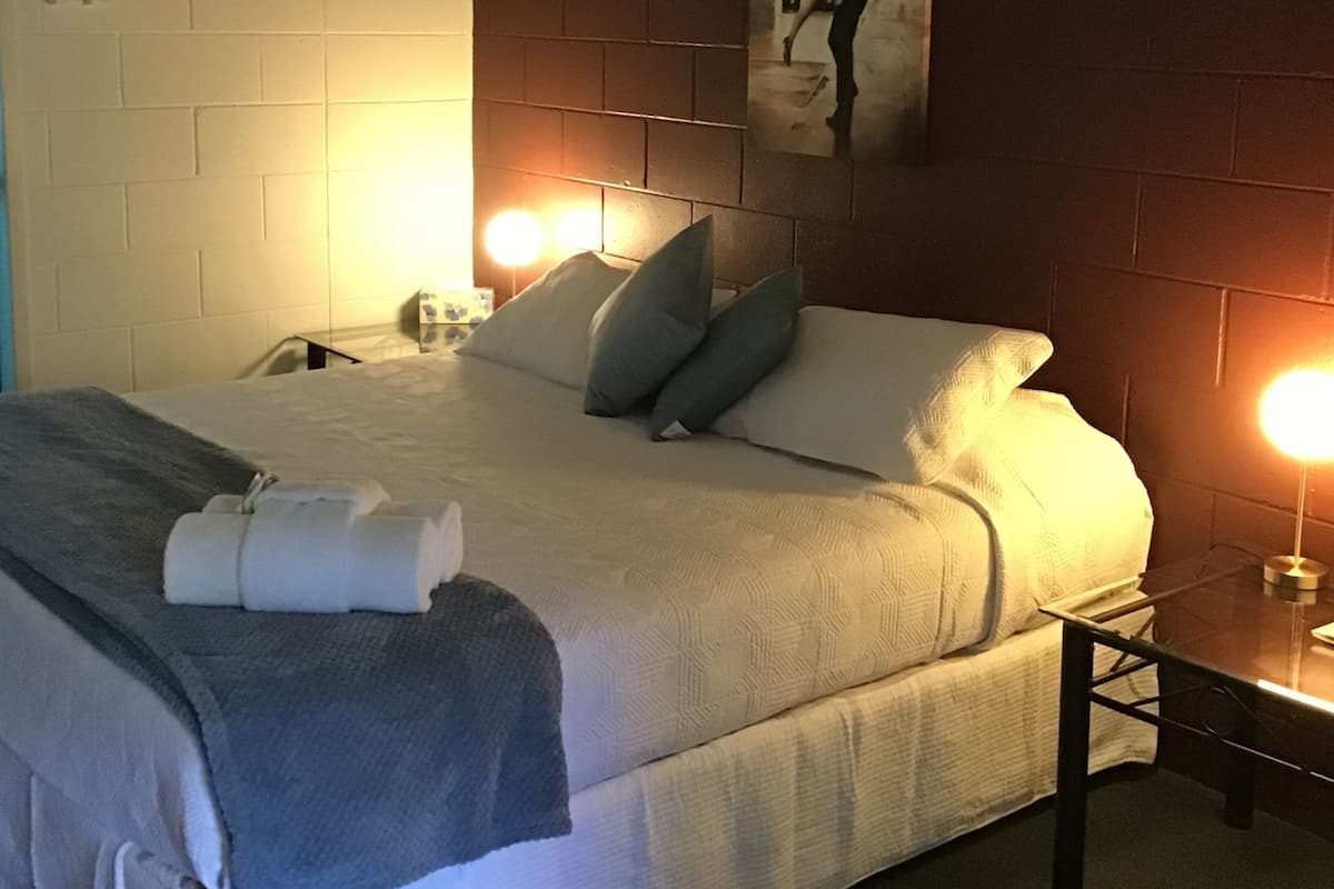 Une chambre d’hôtel équipée d’un lit, d’oreillers, d’une table de chevet, d’une lampe et d’un climatiseur fixé au mur.