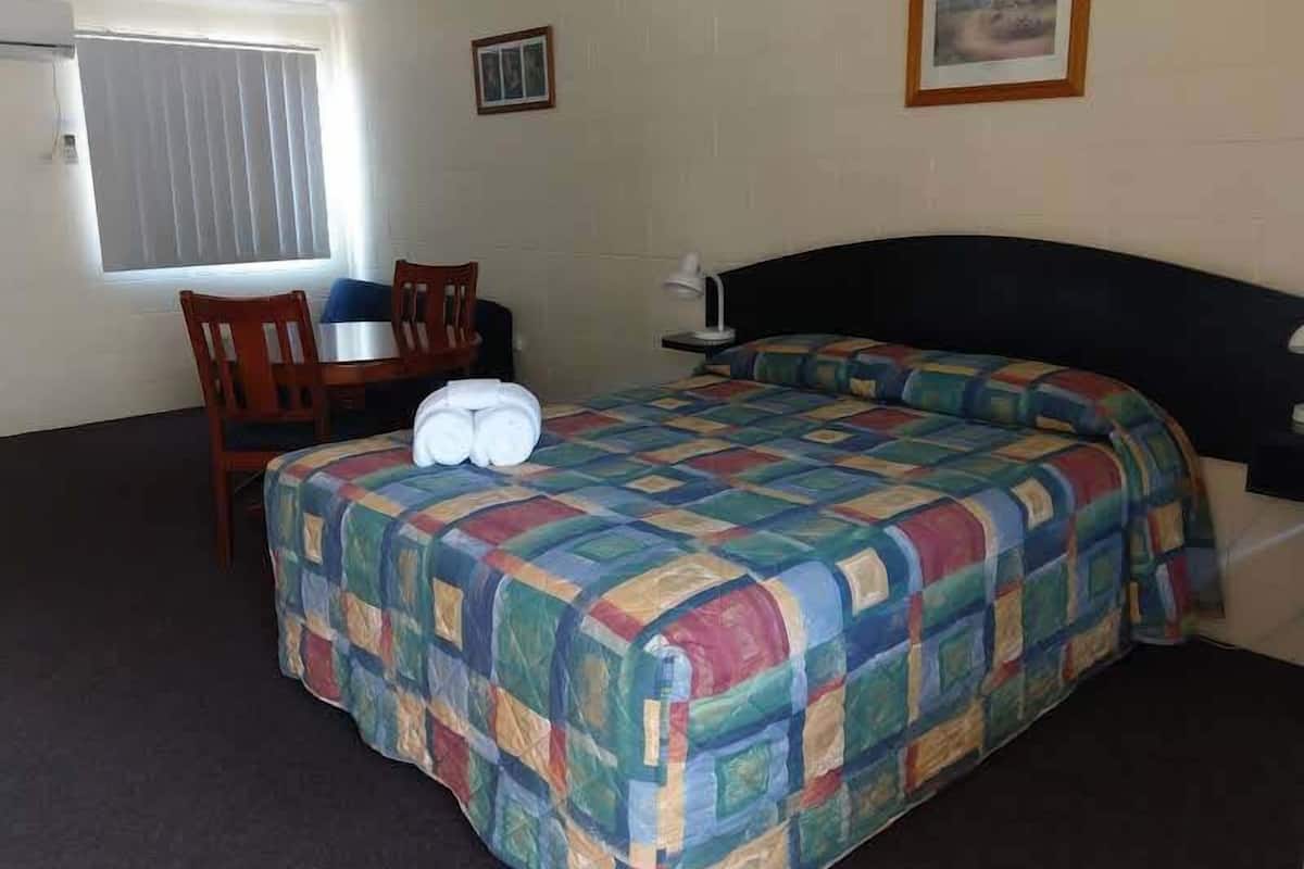 Une chambre d’hôtel avec un lit, un bureau, une chaise et une fenêtre avec des stores.