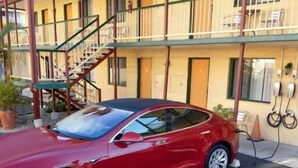 Een rode Tesla staat geparkeerd voor een geel gebouw met een balkon en een trap.