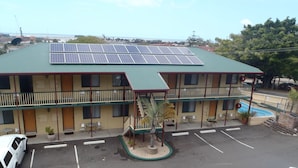 Een motel met een groen dak, zonnepanelen, een zwembad en een parkeerplaats.