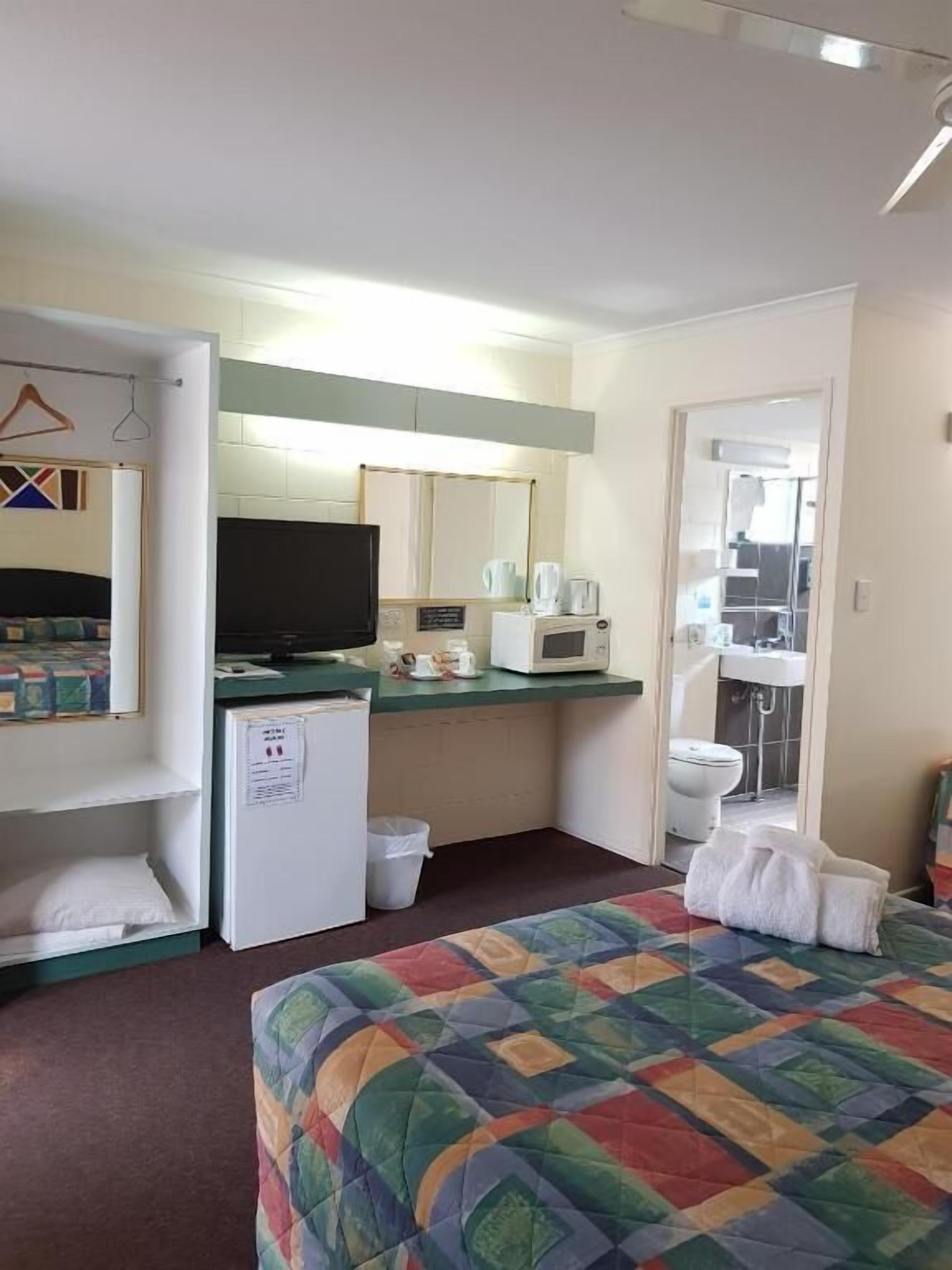 A compact hotel room with a bed, a small kitchenette, a refrigerator, a microwave, a sink, and a toilet.