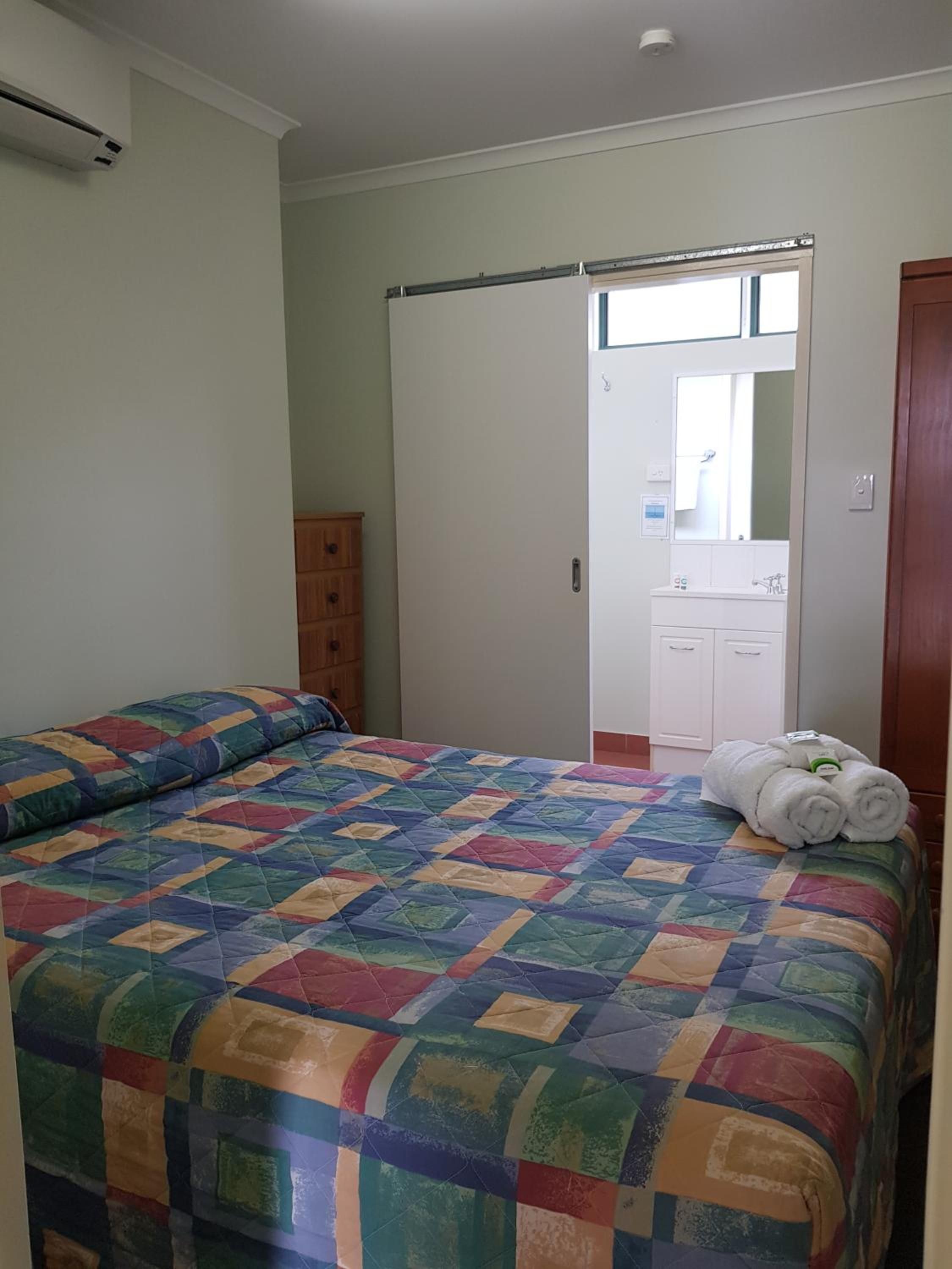 A bedroom with a bed, a wardrobe, a bathroom with a mirror, and a towel on the bed.