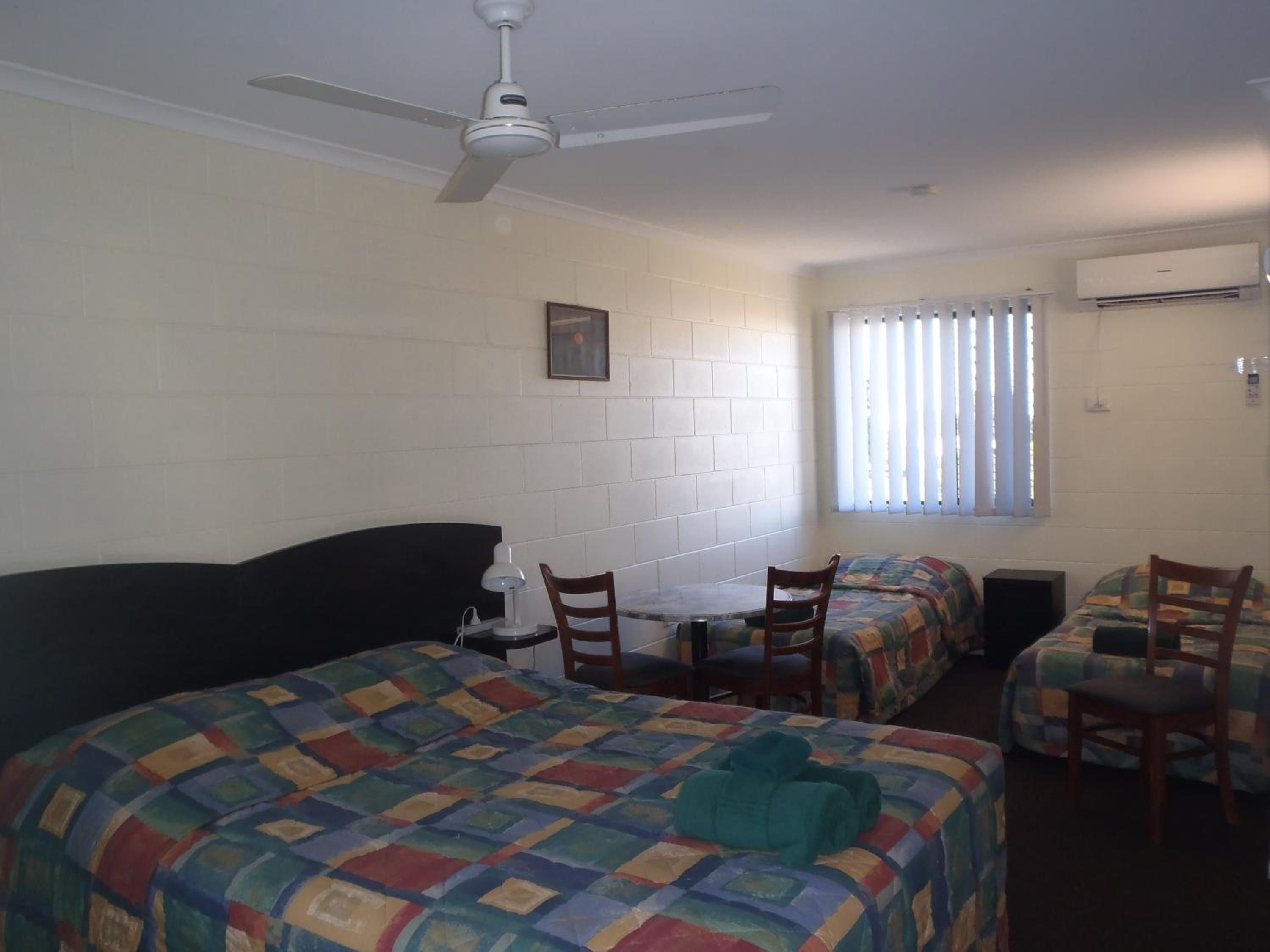 A room with two beds, a table, chairs, a ceiling fan, and an air conditioning unit.