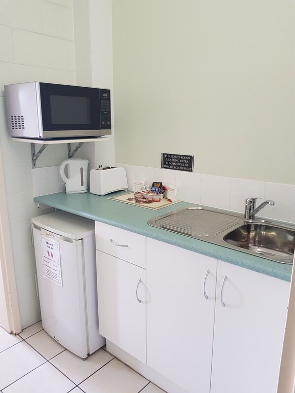 A compact kitchenette with a microwave, toaster, kettle, and a mini fridge. A sign indicates extra cleaning charges for rooms. - Harbour Lodge Motel Gladstone (Gladstone)