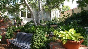 A garden with a bench, potted plants, and a brick wall. - Topiary Haven (West Launceston)