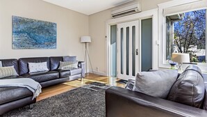 A modern living room with a black leather sofa, a grey rug, and a large abstract painting on the wall. - Topiary Haven (West Launceston)
