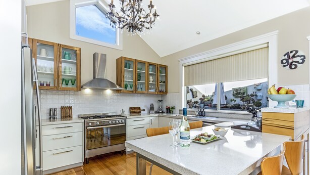 A modern kitchen with a central island, wooden cabinets, and a large window providing natural light. - Topiary Haven (West Launceston)