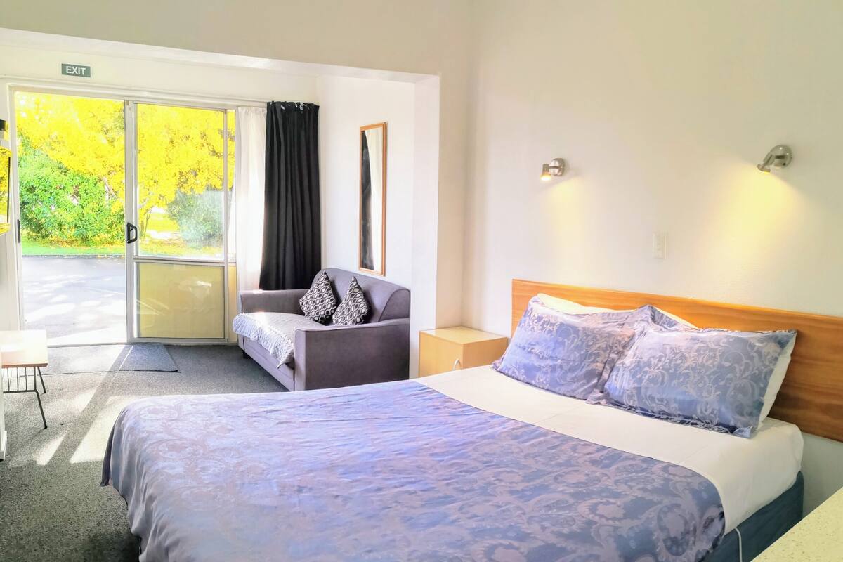 A hotel room with a large bed, a sofa, a desk, and a view of the outdoors.