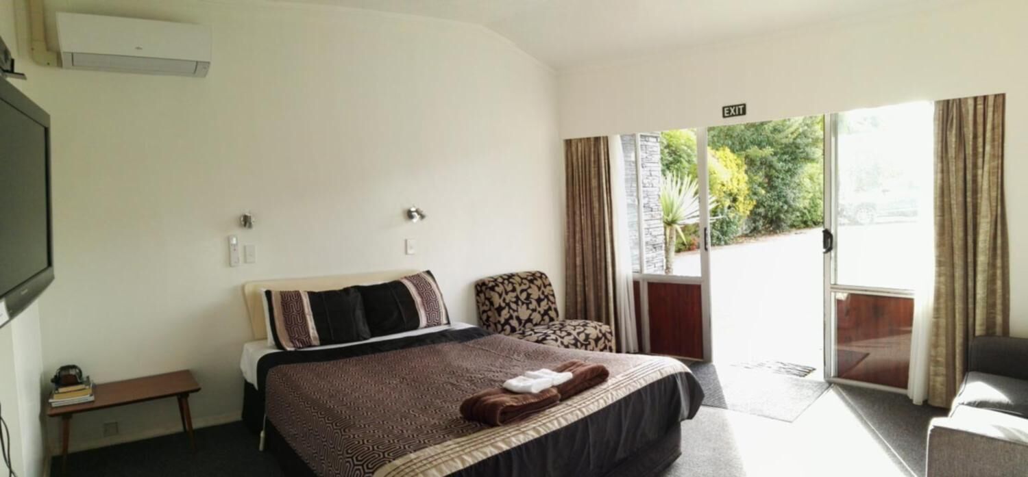 A hotel room with a bed, a chair, a small table, and a sliding glass door to a balcony.