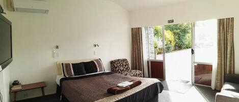 Habitación de hotel con cama, una silla, una mesita y puerta corrediza de cristal a un balcón.