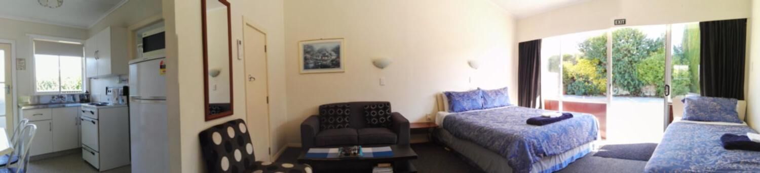 Habitación de hotel con kitchenette, dos camas, sofá y un ventanal con vistas a zonas verdes.