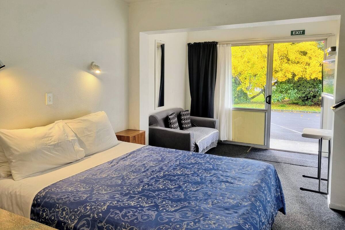 A hotel room with a bed, a chair, and a view of the outdoors.