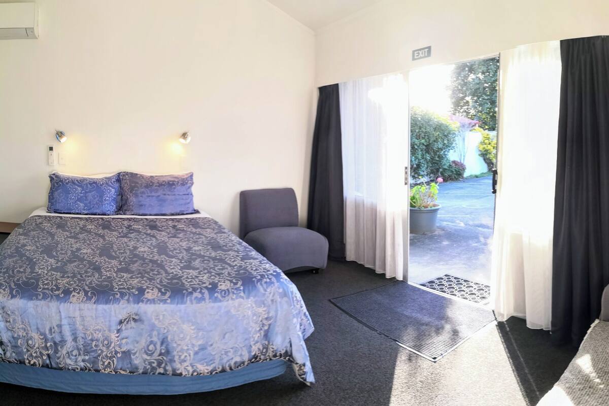 A bedroom with a bed, a chair, a sofa, and a view of the outdoors through a door.