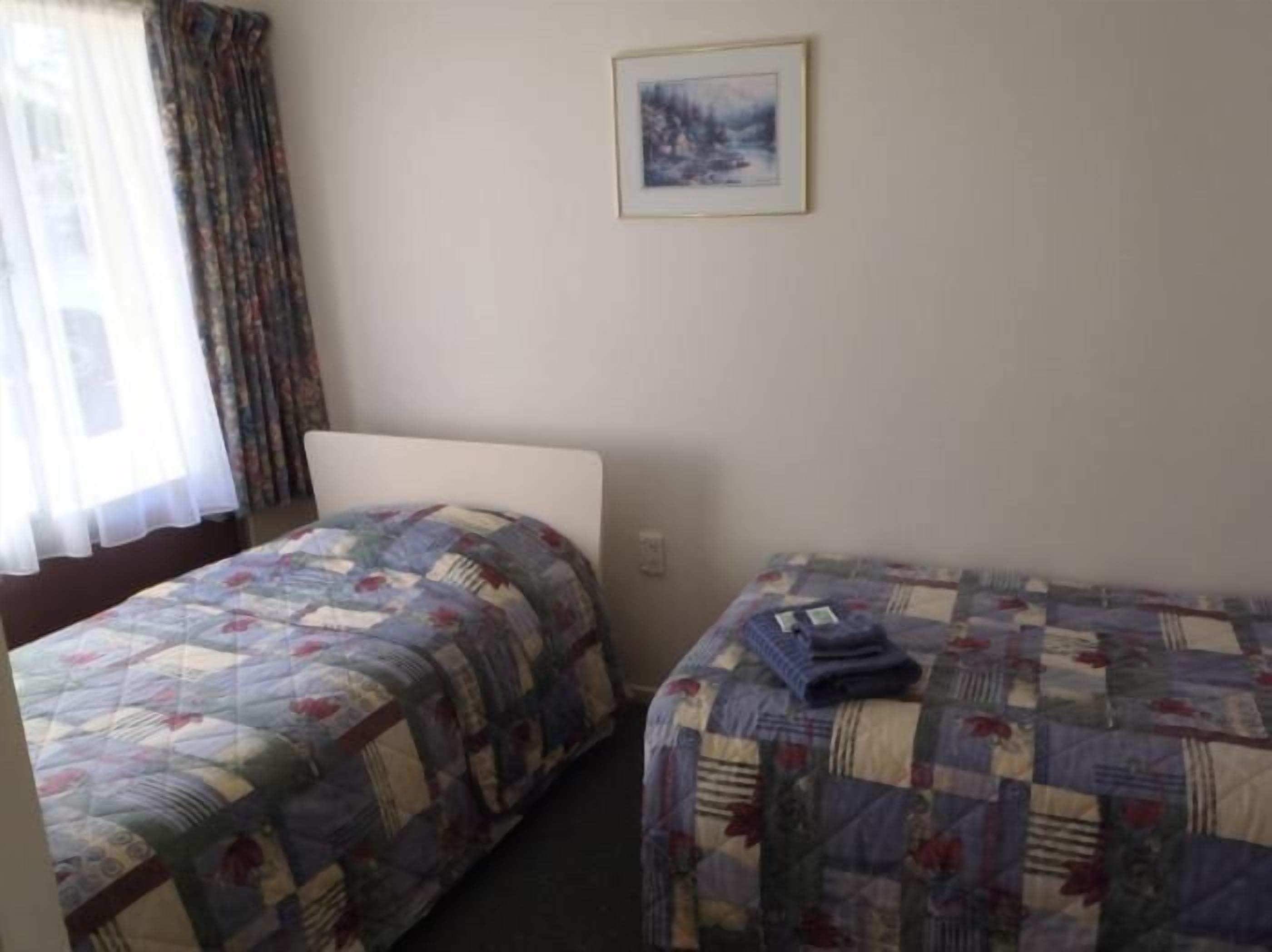 A room with two beds, each with a quilted bedspread. There is a framed picture on the wall above the beds.