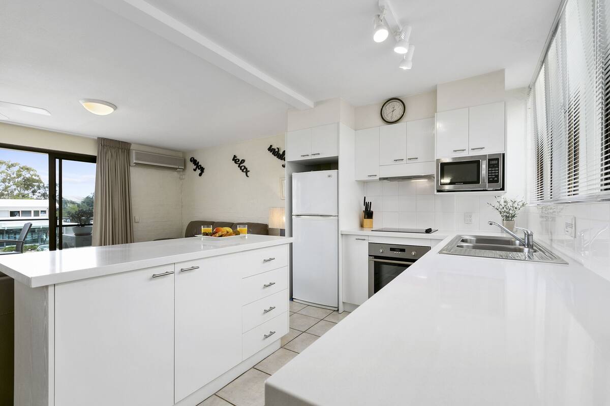 A modern kitchen with white cabinetry, a built-in oven, a microwave, and a large island with a sink.