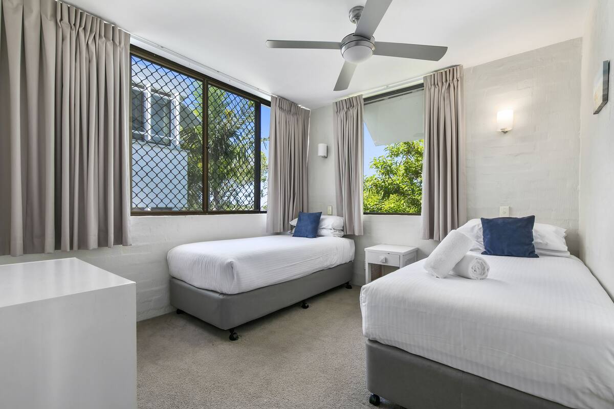 A hotel room with two beds, a ceiling fan, and large windows with curtains.