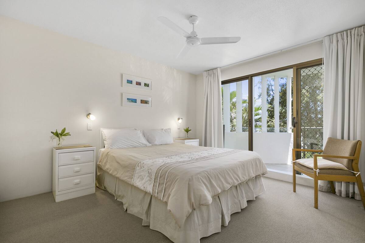 A bedroom with a bed, bedside tables, a chair, and a large window with curtains.