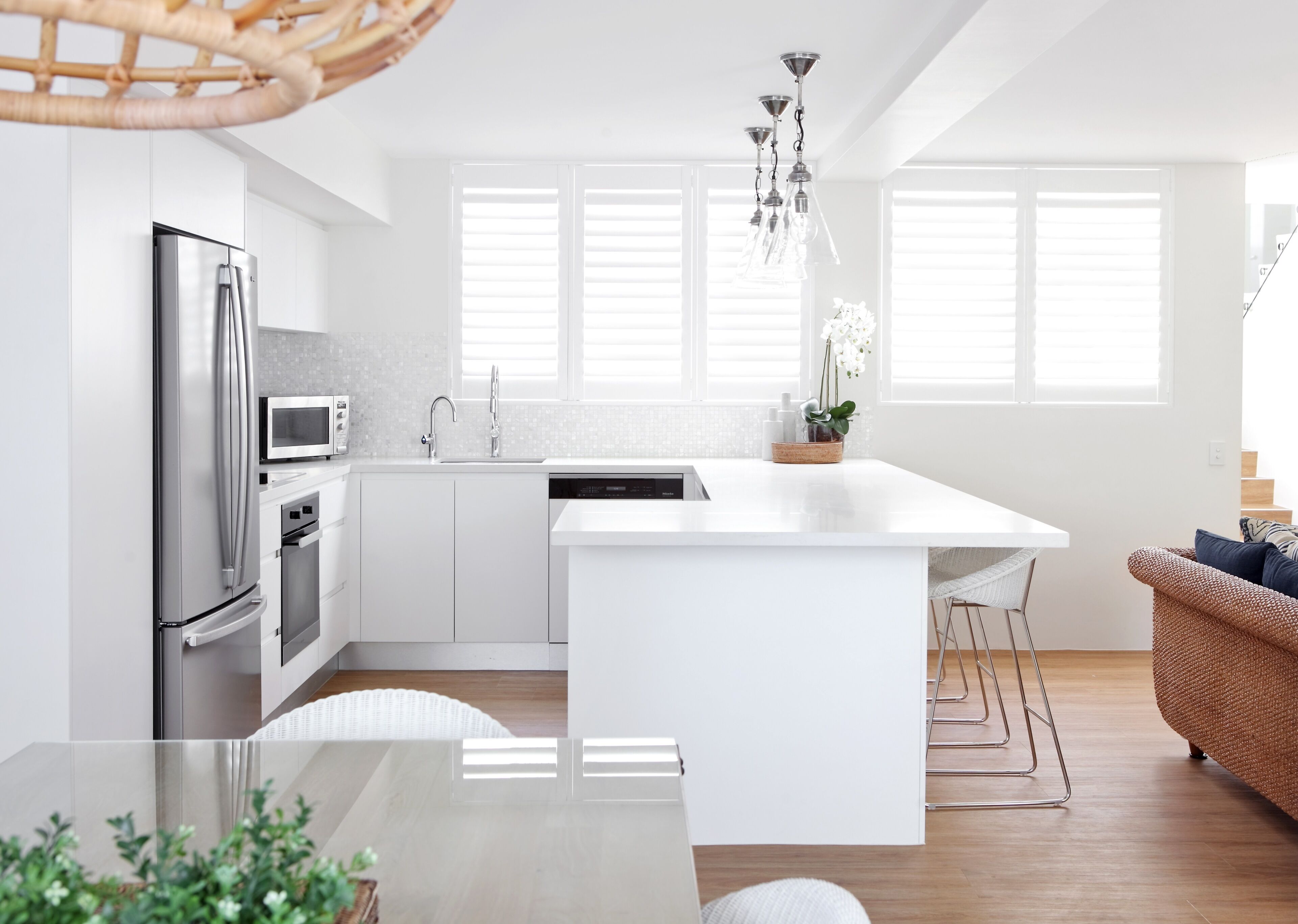 Een moderne keuken met een centraal eiland, roestvrijstalen apparatuur en een rieten stoel.