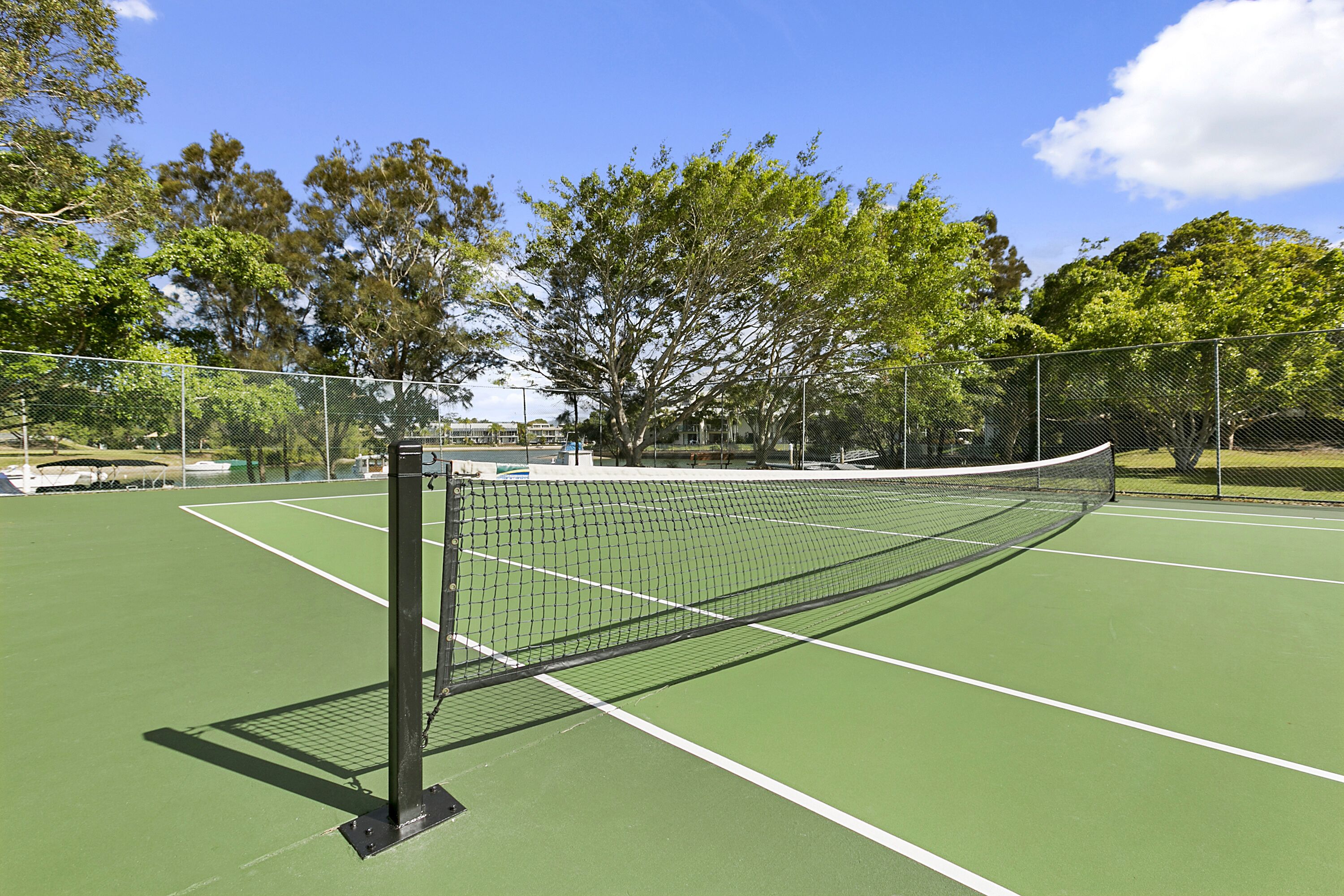 A tennis court with a net, surrounded by trees and a fence.