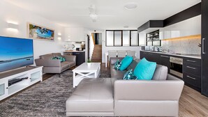 En moderne stue med et fladskærms-tv, grå sofaer og en trappe, der fører op til et køkken.