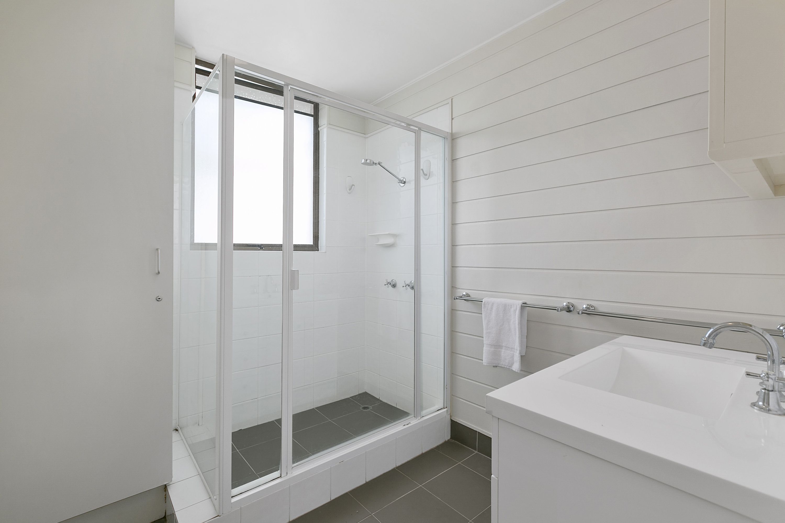 A modern bathroom with a glass-enclosed shower, a white sink, and a window.