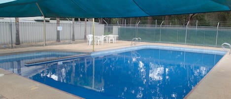 A swimming pool with a blue water surface, surrounded by a fenced area, and a shaded canopy overhead.
