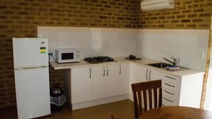 A compact kitchen with white cabinets, a microwave, a stove, and a sink. - Acclaim Swan Valley Tourist Park (West Swan)