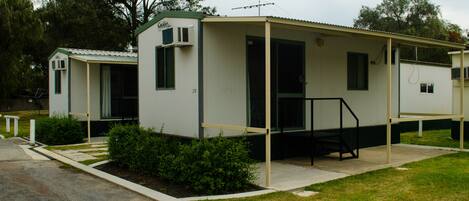 A row of mobile homes with a covered porch and a small garden area in front.