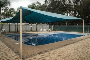 A swimming pool with a canopy, surrounded by a fence, and white chairs. - Acclaim Swan Valley Tourist Park (West Swan)