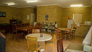 A library with multiple wooden tables and chairs, a pool table, and a brick wall with bookshelves. - Acclaim Swan Valley Tourist Park (West Swan)