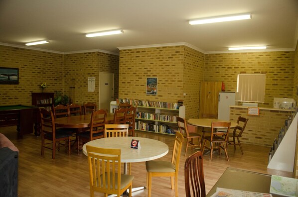 A library with multiple wooden tables and chairs, a pool table, and a brick wall with bookshelves. - Acclaim Swan Valley Tourist Park (West Swan)