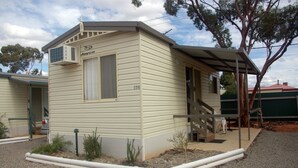 Ein Bungalowmobilheim mit überdachter Veranda, einem kleinen Garten und der Nummer 104 an der Seite.