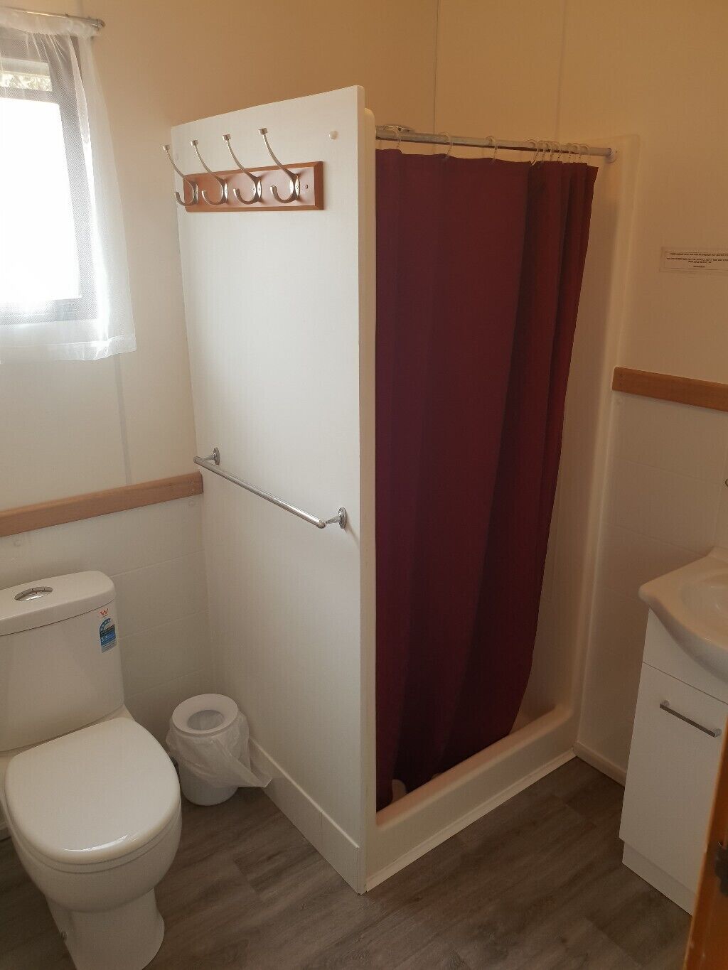 A bathroom with a white toilet, a shower with a wooden door, and a wooden vanity.