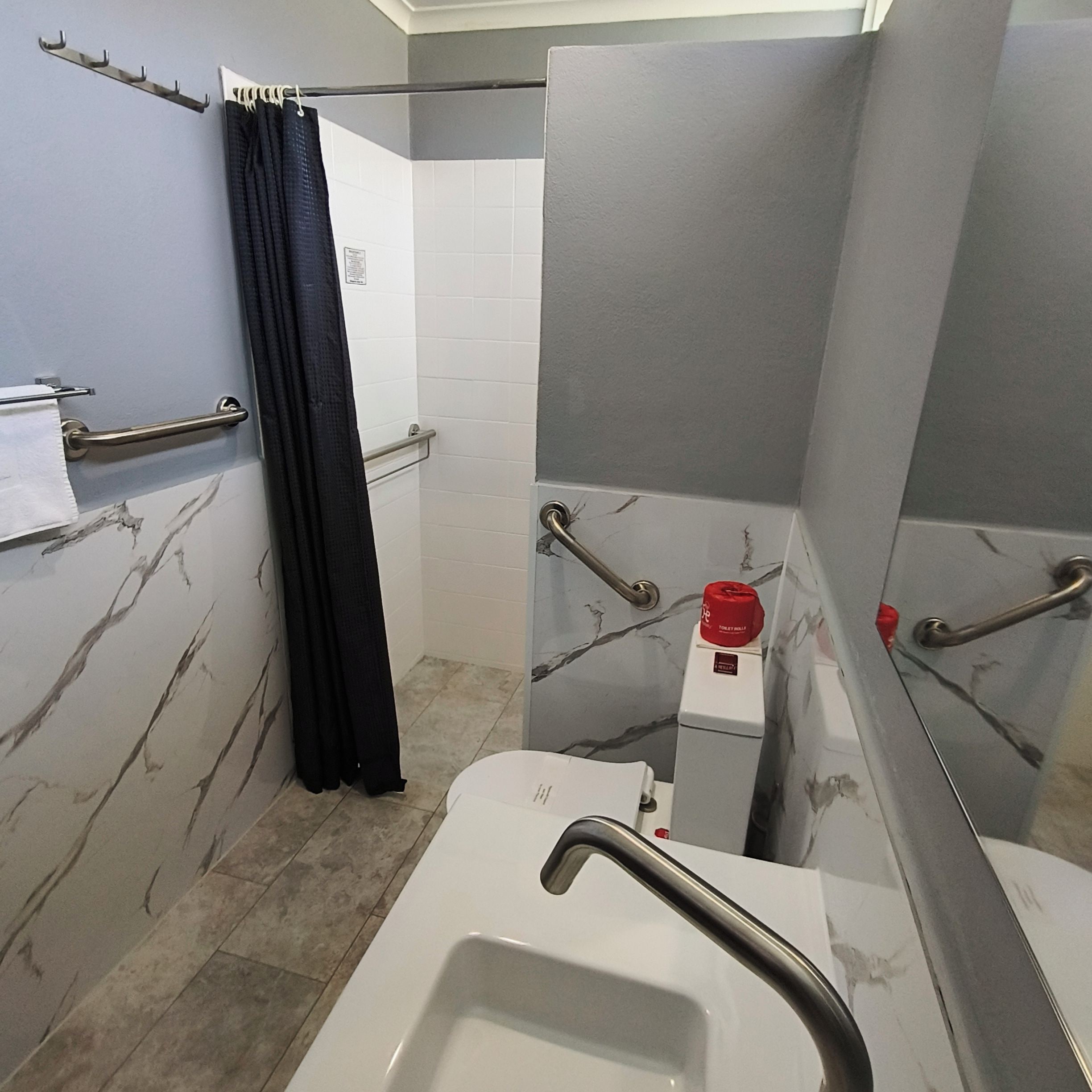 A bathroom with a white sink, a towel rack, a shower curtain, and a handrail.