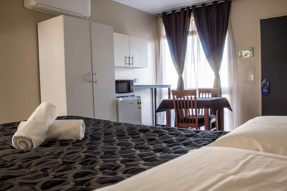 Quarto de hotel com uma cama, uma escrivaninha com micro-ondas, uma cadeira e um guarda-roupa.