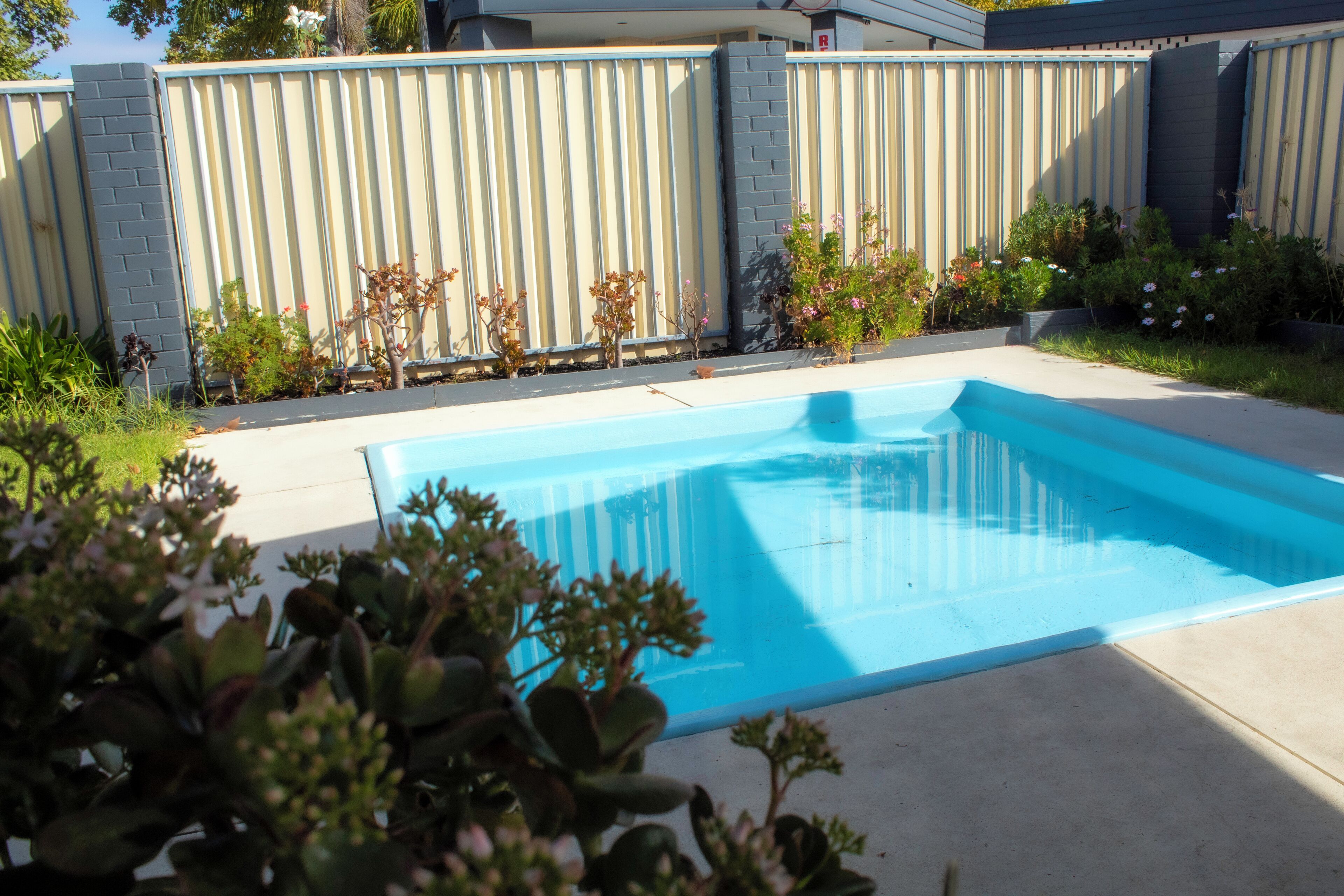 Una piscina rectangular de color azul claro, rodeada por una solana de concreto y una cerca de metal.