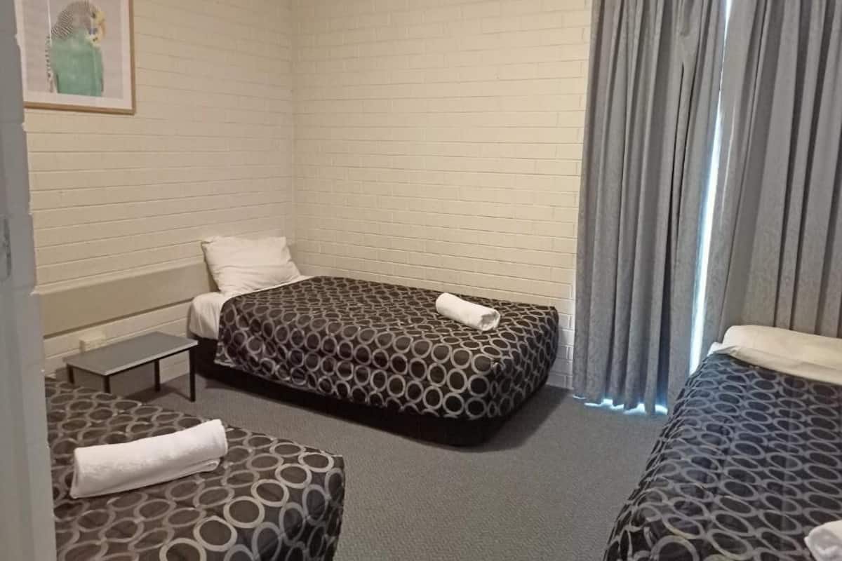 Quarto de hotel com duas camas de solteiro, uma mesinha, uma cadeira e um quadro na parede.