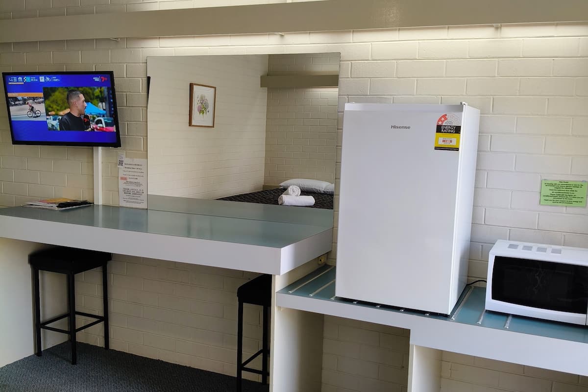 Uma cozinha compacta com geladeira Hisense, micro-ondas, TV exibindo um evento de ciclismo e um pequeno quadro na parede.
