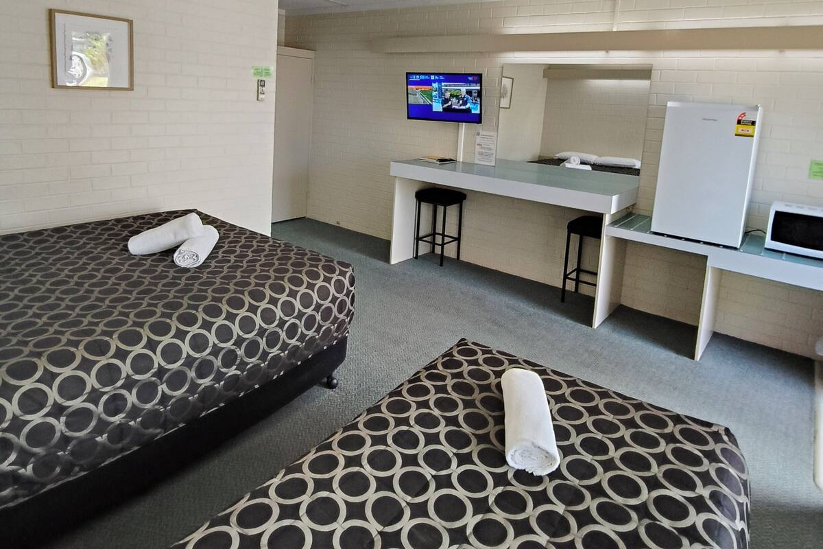 Quarto de hotel com duas camas, uma escrivaninha, televisão e frigorífico.