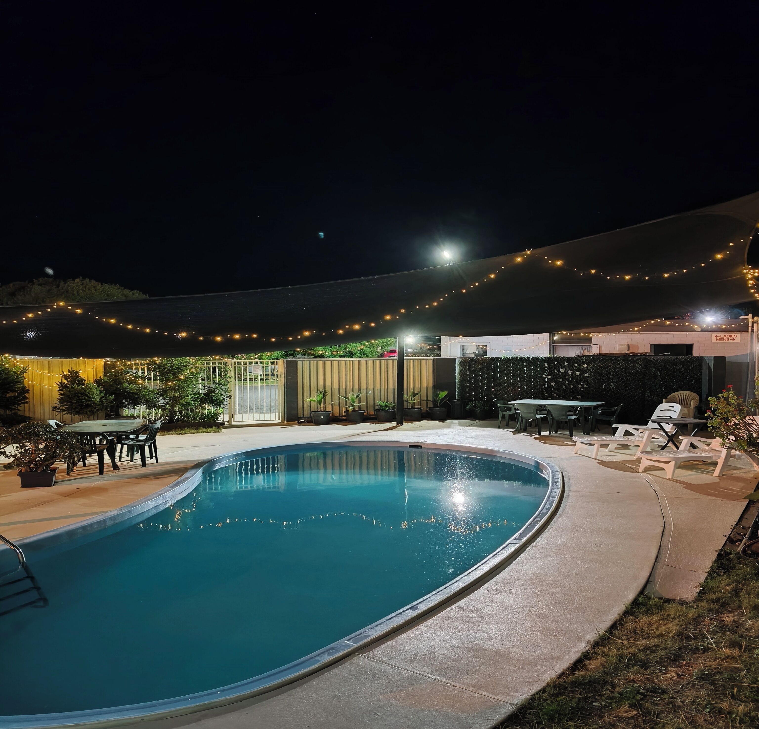 A swimming pool with a surrounding patio area, outdoor seating, and string lights.