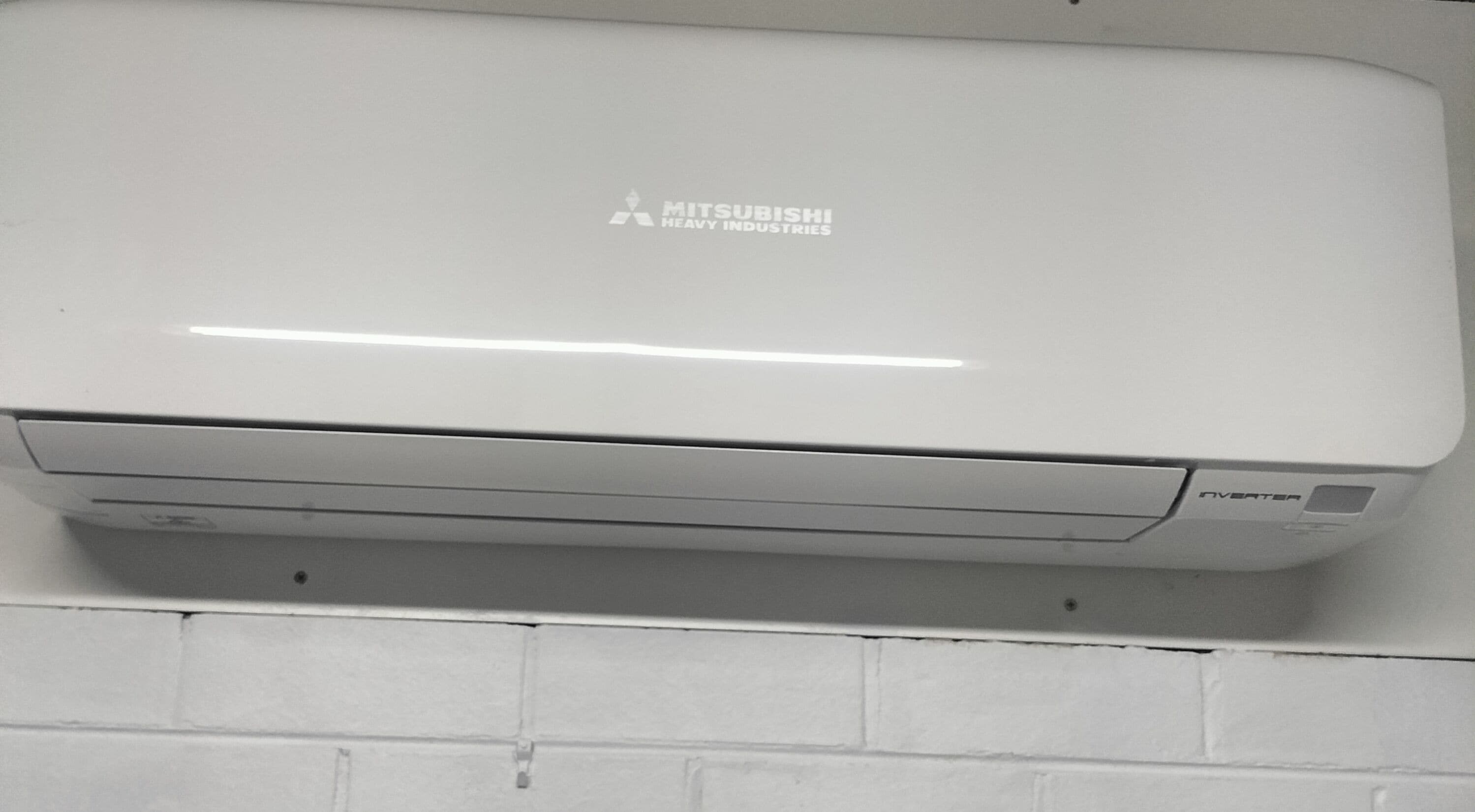 Un equipo de aire acondicionado Mitsubishi instalado en una pared de ladrillo blanco.