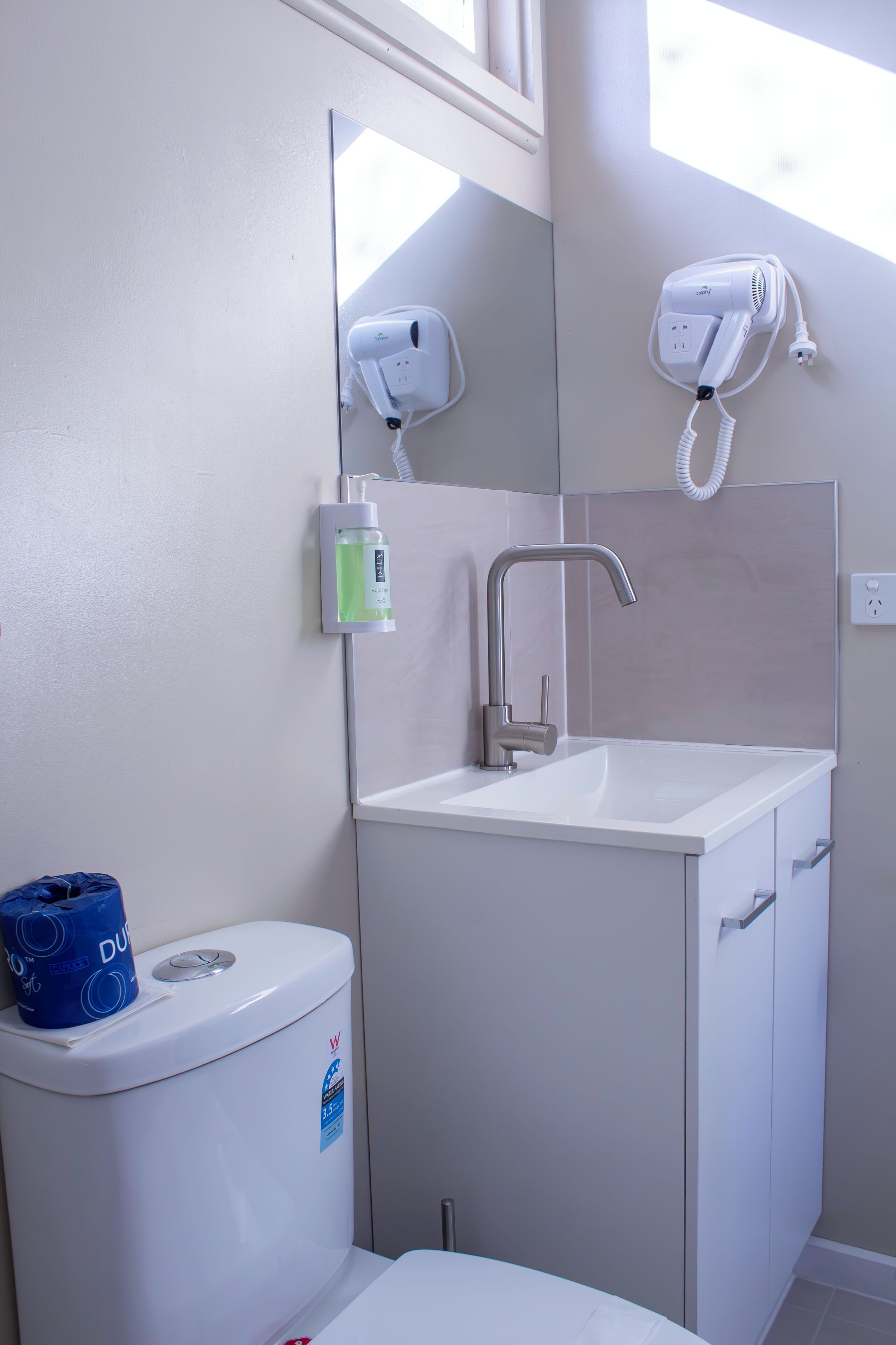 Un baño con lavamanos blanco, un espejo, secador de pelo y un inodoro.