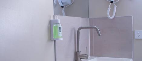 Un baño con lavamanos blanco, un espejo, secador de pelo y un inodoro.