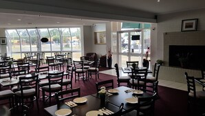 A restaurant with multiple tables and chairs, large windows, and a fireplace. - Wangaratta Motor Inn (Wangaratta)