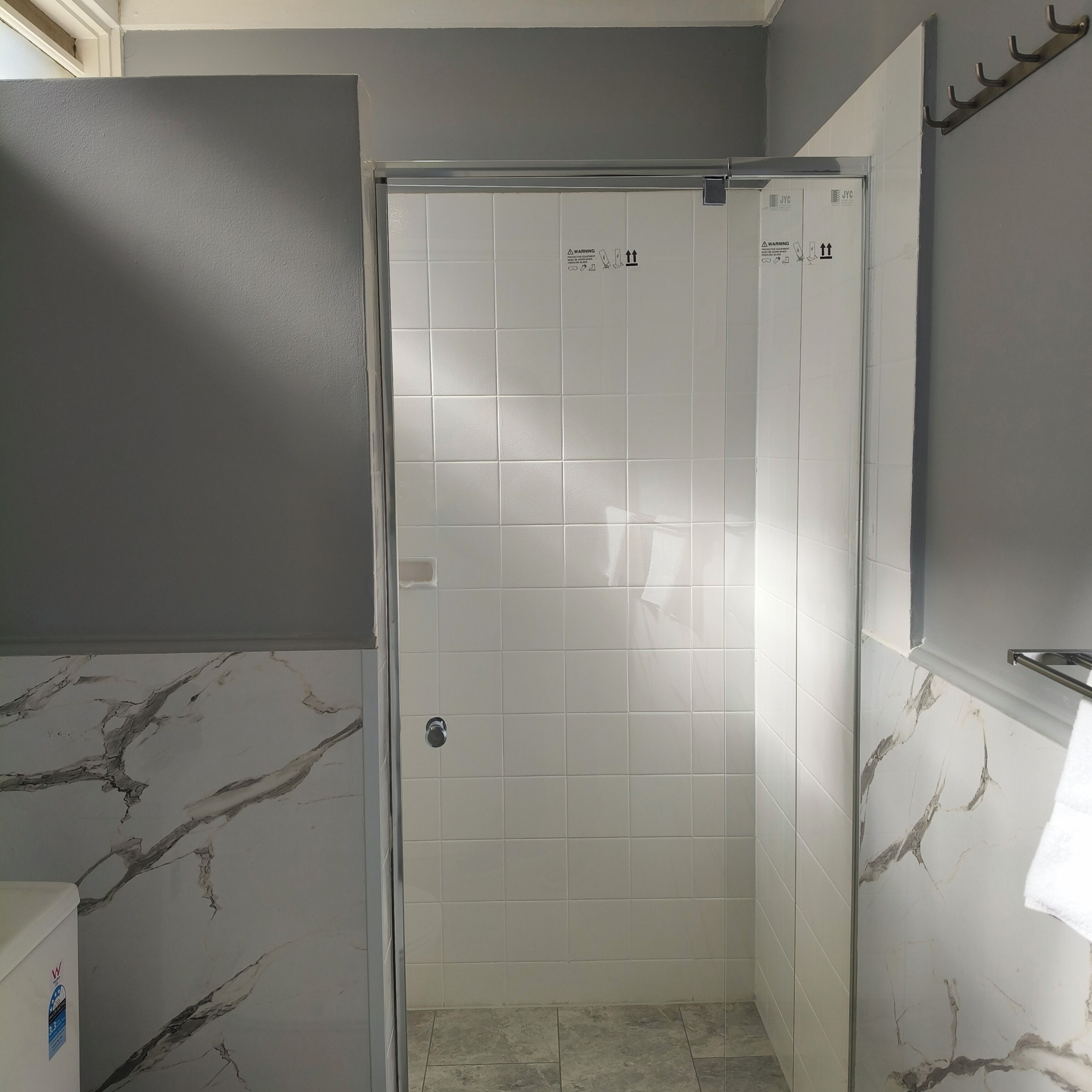 A bathroom with a shower area, tiled walls, and a marble-patterned wall.
