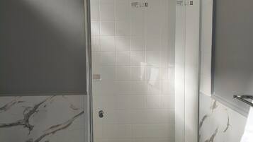 A bathroom with a shower area, tiled walls, and a marble-patterned wall.