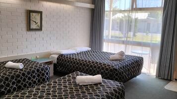 Une chambre d’hôtel avec deux lits, une fenêtre avec des rideaux, un mur décoré d’un motif en briques et une horloge.